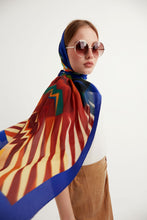 Load image into Gallery viewer, Discover the harmony of tradition and contemporary elegance with this timeless crepe silk shawl. This large shawl radiates warmth through its red, yellow and blue sunset colours, evoking a vibrant energy and life-giving power.
